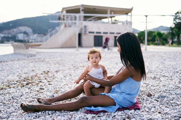 Petite fille assise sur les genoux de maman sur la plage