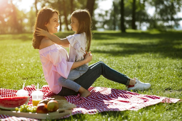 Petite fille assise sur les genoux de sa mère dans le parc Petite fille assise sur les genoux de sa mère dans le parc