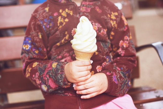 Petite fille assise avec une grosse corne de glace à la vanille.
