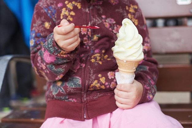 Petite fille assise avec une grosse corne de glace à la vanille.