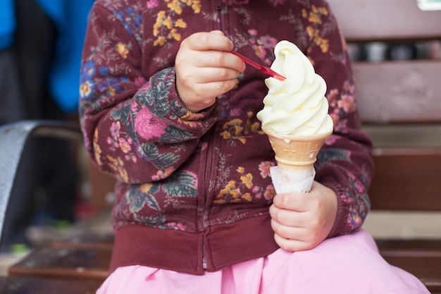 Petite fille assise avec une grosse corne de glace à la vanille.