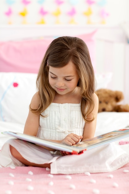 Petite fille assise sur le lit en lisant un livre