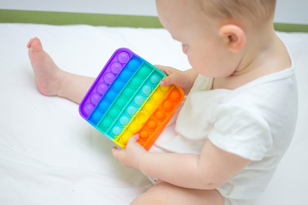 Petite fille assise à la maison sur le lit, jouant au nouveau jouet anti-stress Pop-it, populaire auprès des enfants. Idée de développement d'enfant.