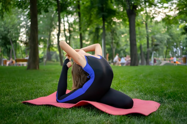 Une petite fille assise sur la pelouse dans le parc effectue des backbends elle fait des éléments de yoga pour étirer son dos