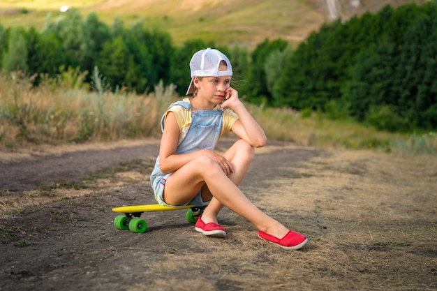 Petite fille assise sur une planche à roulettes à la campagne