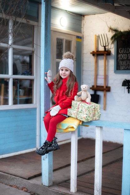 petite fille assise sur le porche de la maison avec des cadeaux de noël et un ours en peluche