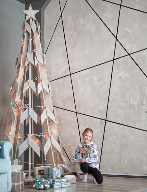 Petite fille assise près d'un arbre de Noël stylisé. le concept de vacances en famille