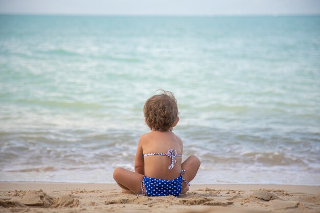 Petite fille assise sur le sable et jouant avec des jouets sur la plage de la mer dans une chaude journée d'été ensoleillée