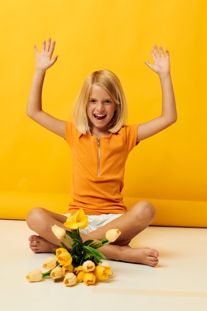Petite fille assise sur le sol avec un bouquet de fleurs fond jaune