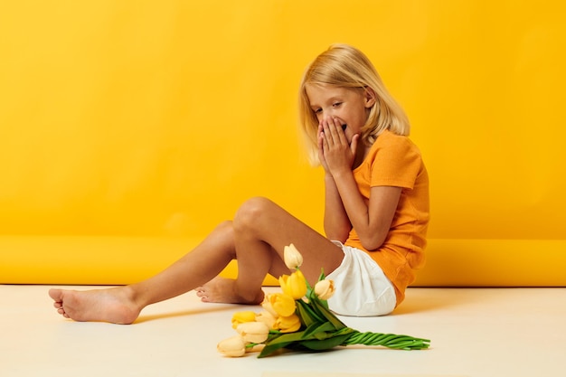 Petite fille assise sur le sol avec un bouquet de fleurs fond jaune