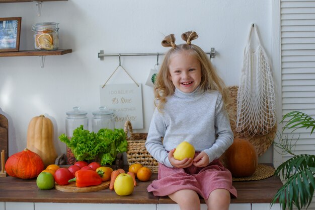 Petite fille assise à la table de la cuisine tenant une pomme en souriant
