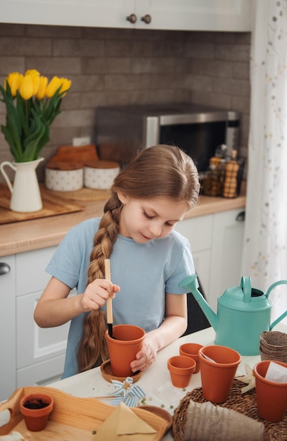 Petite fille assise à la table à la maison semant des graines dans des pots de fleurs