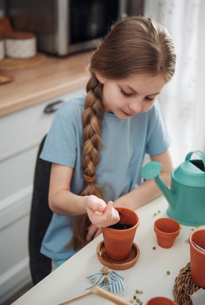 Petite fille assise à la table à la maison semant des graines dans des pots de fleurs