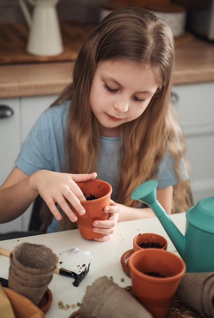 Petite fille assise à la table à la maison semant des graines dans des pots de fleurs