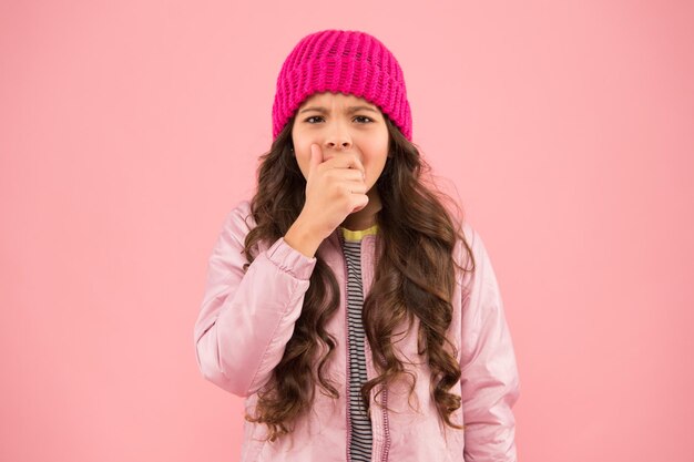 Petite fille attraper la toux pas de grippe cet hiver porter des vêtements chauds pendant la saison froide activité de vacances d'hiver petite beauté fond rose style de mode enfant bonnet tricoté et manteau bouffant grippe hivernale