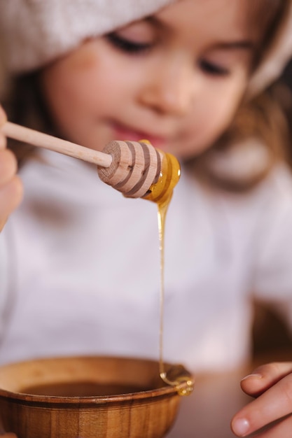 Petite fille au bonnet rouge mangeant du miel dans une cuisine décorée de guirlandes lumineuses à l'ambiance de Noël