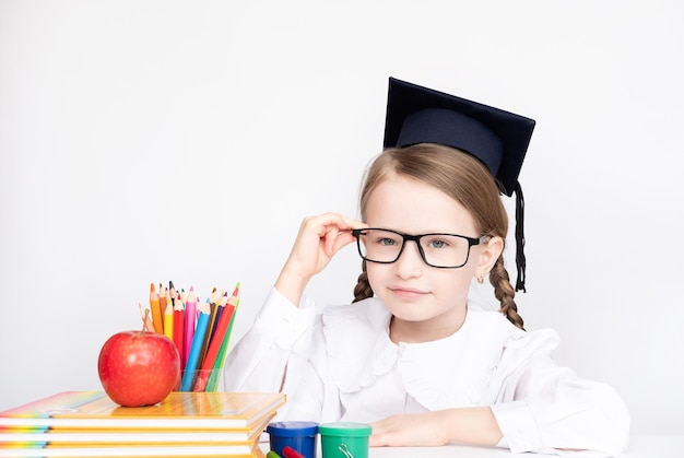 Petite fille au chapeau d'étudiant et lunettes tenant un tableau noir vide sur fond blanc retour à l'école