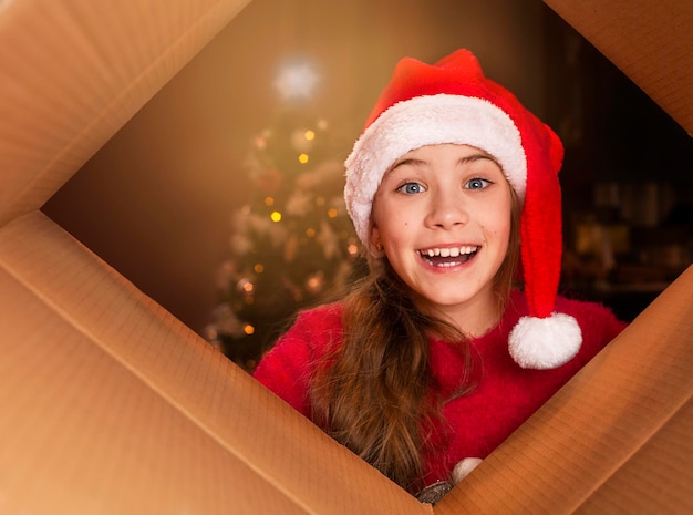 Petite fille au chapeau de Père Noël ouvrant une boîte en carton et regardant la caméra