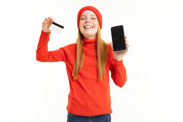 Petite fille au chapeau rouge se réjouit du nouveau téléphone tenant une carte de crédit à la main