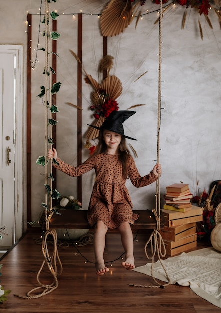 Une petite fille au chapeau de sorcière est assise sur une balançoire et se balance