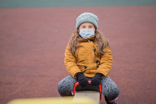 Petite fille au masque médical sur balançoire.