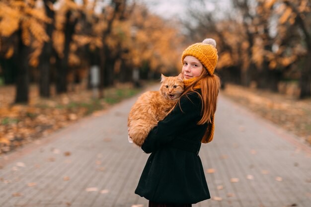 Petite fille au visage de taches de rousseur tenant son chat dans le parc en automne.