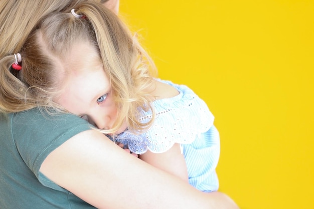 Une petite fille aux cheveux blancs est bouleversée et triste sur l'épaule de sa mère sur fond jaune Les peurs des enfants les ressentiments les relations mère-enfant La maternité mère-enfant