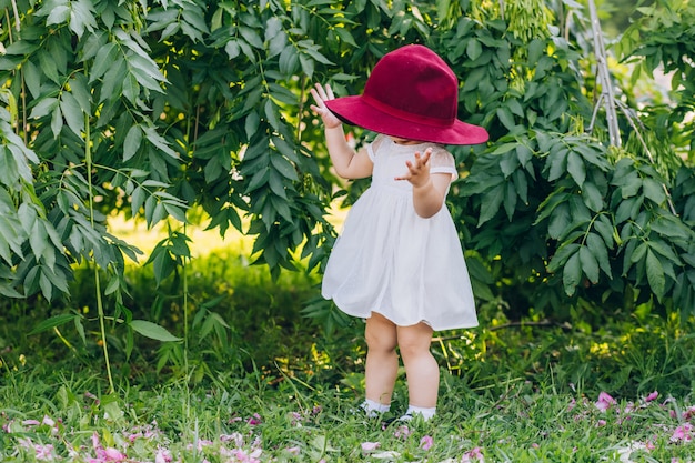 petite fille aux cheveux blonds dans une robe blanche et le chapeau rouge de la mère dans le parc journée d'été ensoleillée