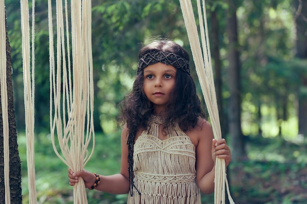 Photo petite fille aux cheveux bouclés foncés habillée en indigène dans la forêt