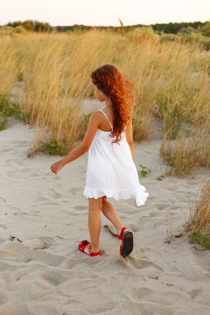 Petite fille aux cheveux bouclés marchant sur la plage