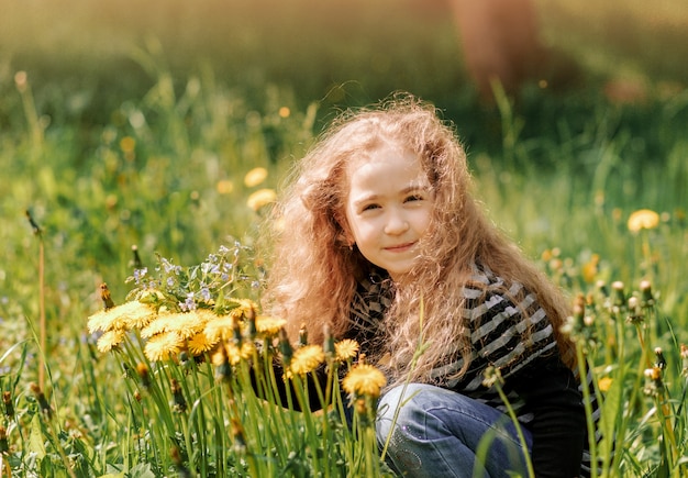 Une petite fille aux cheveux bouclés recueille des fleurs dans le parc en été