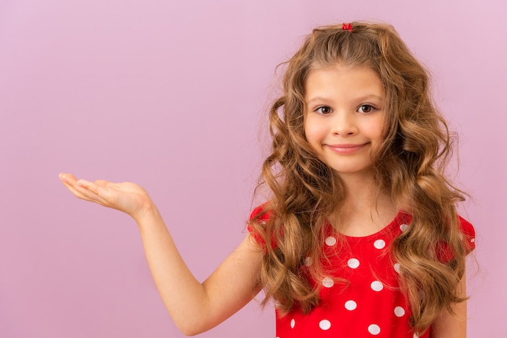 Photo une petite fille aux cheveux bouclés et sa main sur le côté sur fond rose