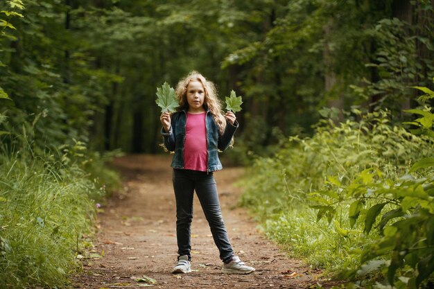 Petite fille aux cheveux bouclés tient des feuilles dans les mains - portrait en plein air, prise de vue au téléobjectif