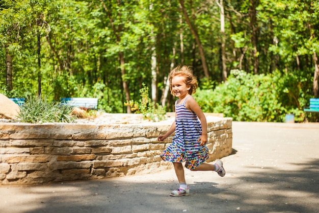 Une petite fille aux cheveux courts et en robe joue l'été dans le parc, attrape des bulles de savon, rit, émotions, enfance.