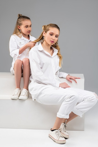 Petite fille aux cheveux longs calme assise derrière sa sœur aînée et faisant sa nouvelle coiffure