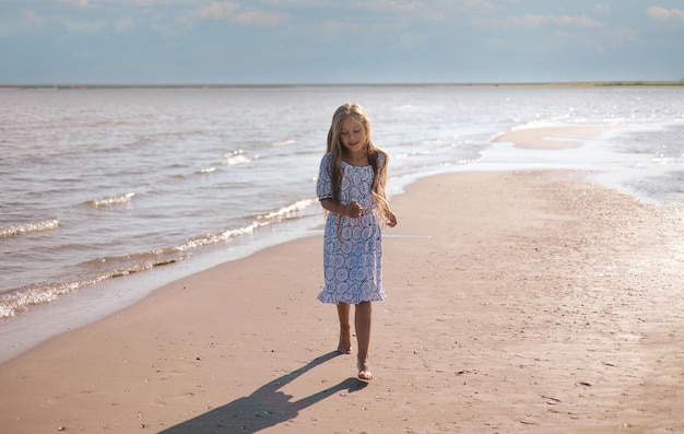 Photo petite fille aux cheveux longs dans une belle robe courant sur la plage pendant les vacances d'été