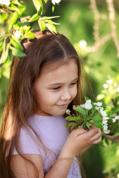 Petite fille aux cheveux longs près d'un arbre en fleurs dans la nature