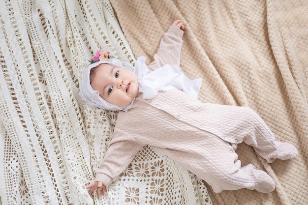 Une petite fille aux couleurs beiges naturelles à la maison est allongée sur le lit et sourit