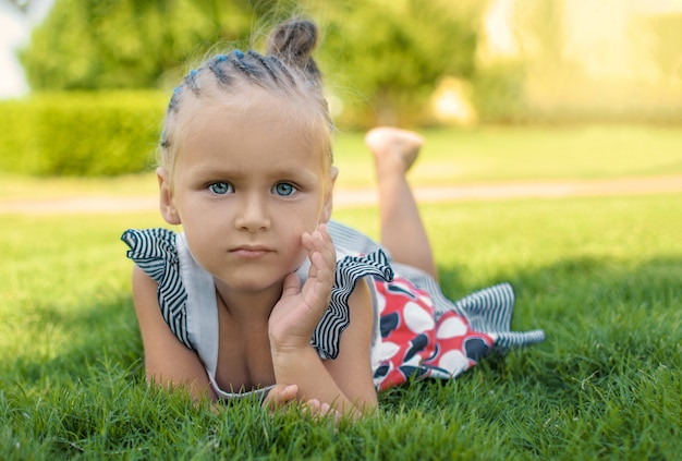 Une petite fille aux yeux brillants se trouve sur l'herbe.