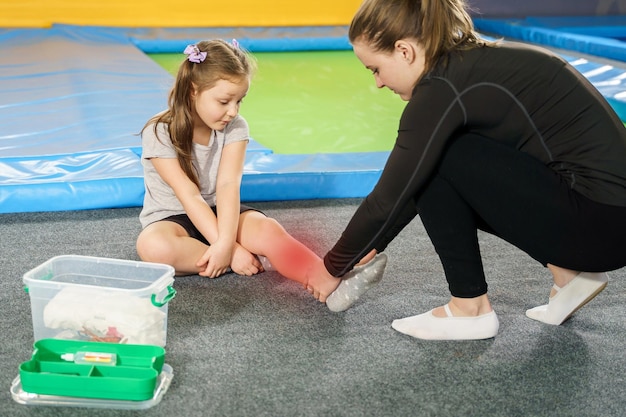 Petite fille ayant des douleurs à la cheville et obtenant de l'aide après avoir sauté sur une tache rouge de trampoline montrant de la douleur