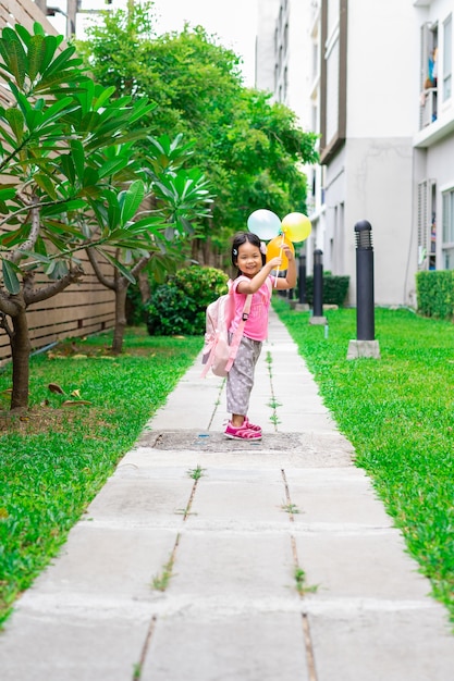 Petite fille avec ballon et sac à dos marchant dans le parc