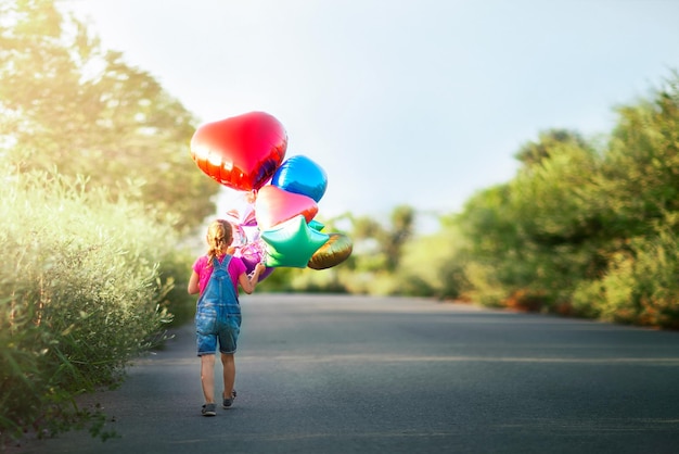 une petite fille avec des ballons avance sur la route