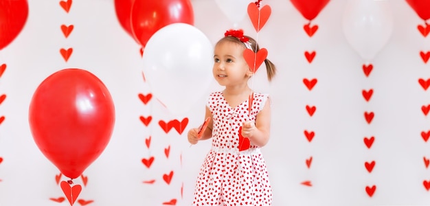 Petite fille avec des ballons et une sucette en forme de cœur regarde pensivement de côté à l'espace de copie