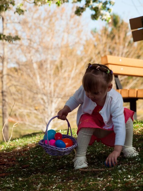 Petite fille en bas âge sur la chasse aux œufs de Pâques dans le parc urbain.