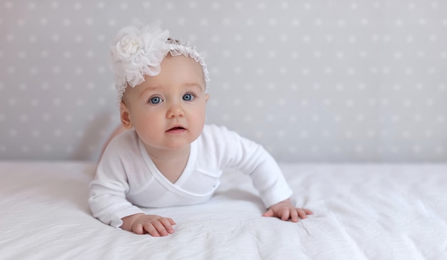 Petite fille en bas âge dans un body blanc allongé sur le lit à la maison en regardant la caméra. Copiez l'espace pour le texte, la maquette, la bannière