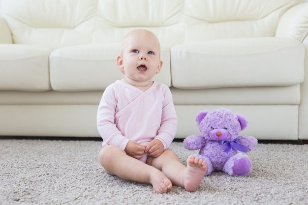 Petite fille de bébé rampant d'un an assis sur le sol dans un salon lumineux et souriant