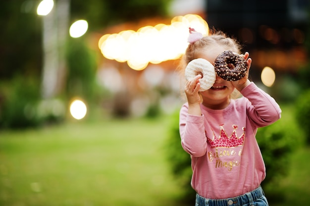 Petite fille avec des beignets au jardin du soir. Nourriture délicieuse et délicieuse de beignets.