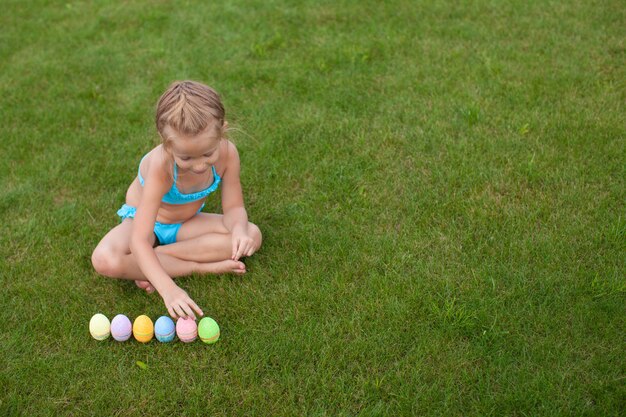 Petite fille belle considère les oeufs de Pâques sur l'herbe verte