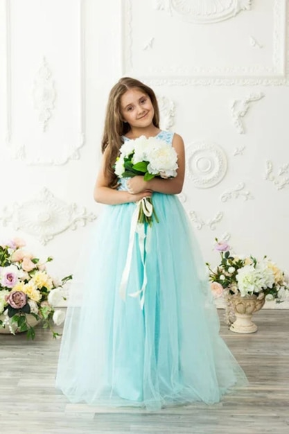 Petite fille belle et mignonne dans une robe turquoise festive à la mode dans un intérieur