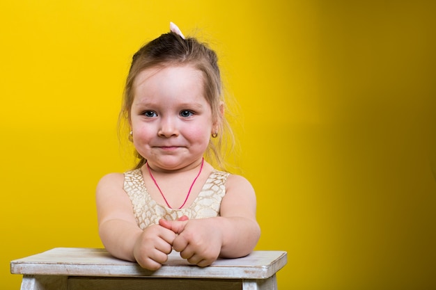 Petite fille avec une belle robe avec chaise sur fond jaune